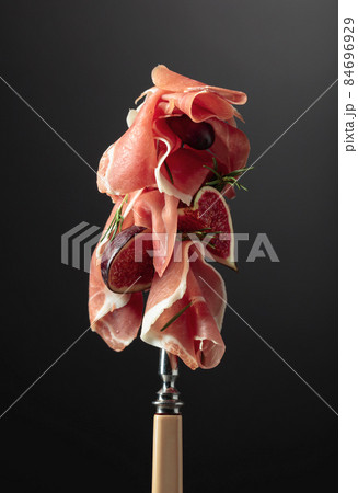 Prosciutto with figs, rosemary, and red olives on a fork. Prosciutto with figs, rosemary, and red olives on a fork. 84696929