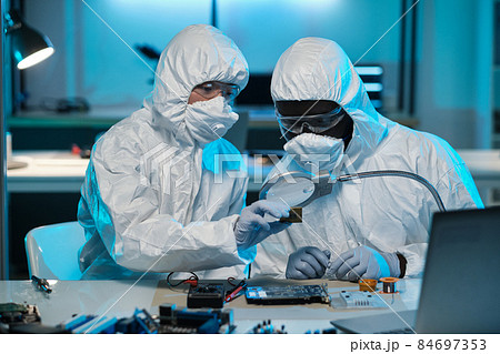 Young Asian woman in coveralls helping colleague with repairment of microchip Young Asian woman in coveralls helping colleague with repairment of microchip 84697353