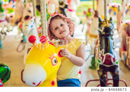 Cute little girl enjoying in funfair and riding on colorful carousel house 84698673