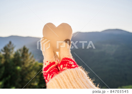 Woman traveler in christmas gloves holding snow in the shape of a heart on a background of mountains with sunbeams. Winter travelling concept Woman traveler in christmas gloves holding snow in the shape of a heart on a background of mountains with sunbeams. Winter travelling concept 84703545