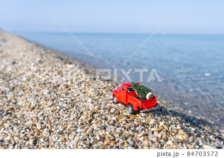 Red retro small car carrying christmas tree on the sea beach shore. Winter holiday concept Red retro small car carrying christmas tree on the sea beach shore. Winter holiday concept 84703572