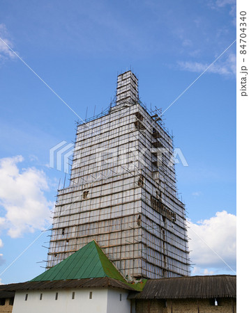 Scaffolding from planks around old bell tower. Background blue sky with clouds. 84704340