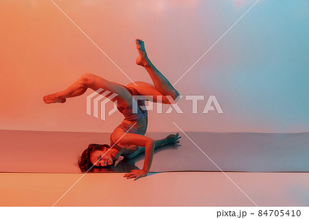 Young flexible, graceful girl, female contemp dancer in art performance isolated on gradient blue orange background in neon 84705410