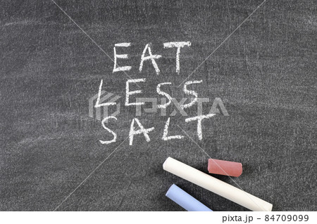 Colored pieces of chalk on a blackboard. Eat Less Salt 84709099