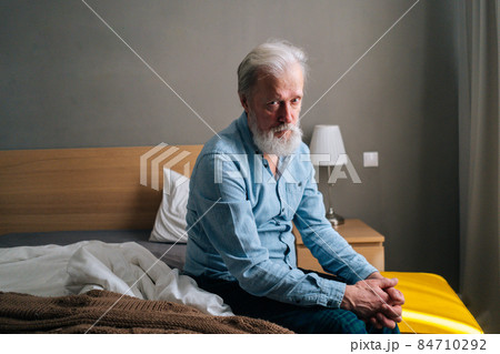 Depressed gray-haired worried senior old adult male sitting alone in nursing home thinking of lonely life looking at camera. 84710292