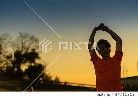 夕焼けの中ストレッチをする中年男性のシルエット 夕焼けの中ストレッチをする中年男性のシルエット 84711818