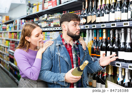 Young family couple deciding what sparkling wine to buy in grocery store Young family couple deciding what sparkling wine to buy in grocery store 84716386