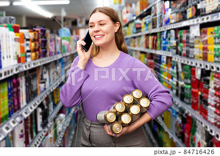 woman buys canned beer in hypermarket and talking on mobile phone 84716426