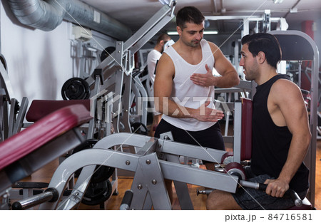Man helping friend on fitness machine in gym 84716581