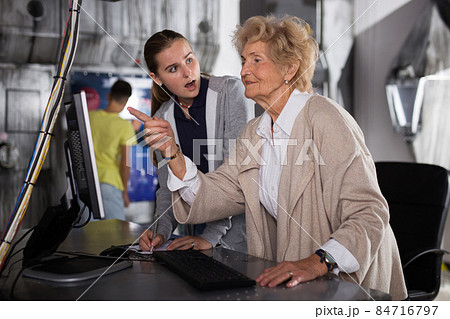 Girl and an elderly grandmother are trying to solve puzzle using computer to get out of quest during corporate event Girl and an elderly grandmother are trying to solve puzzle using computer to get out of quest during corporate event 84716797
