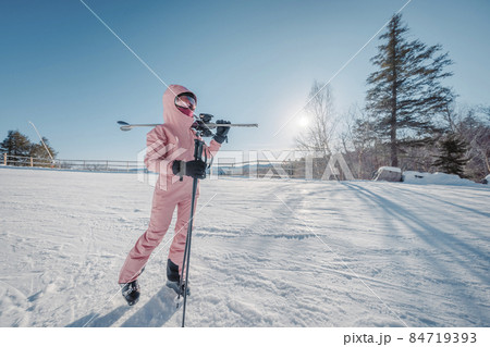 Winter Ski. Skiing portrait of woman alpine skier holdings skis wearing helmet, cool ski goggles, hardshell winter jacket and ski gloves on cold day in front of snow covered trees on ski trail slope 84719393