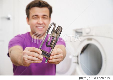 repairman of washing machine holds old tubular electric heater  84720719