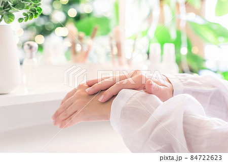 Woman applying daily cream on her hand sitting near dressing table with make up accessories. Reflection of christmas tree, light bulbs in table mirror. Woman applying daily cream on her hand sitting near dressing table with make up accessories. Reflection of christmas tree, light bulbs in table mirror. 84722623