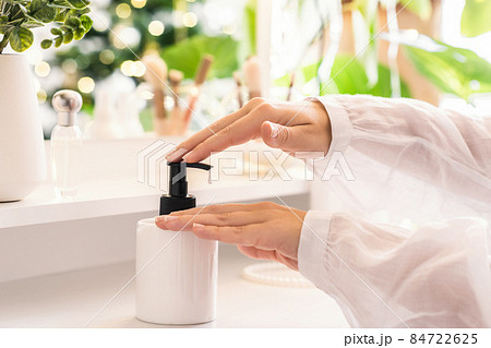 Woman applying daily cream on her hand sitting near dressing table with make up accessories. Reflection of christmas tree, light bulbs in table mirror. Woman applying daily cream on her hand sitting near dressing table with make up accessories. Reflection of christmas tree, light bulbs in table mirror. 84722625