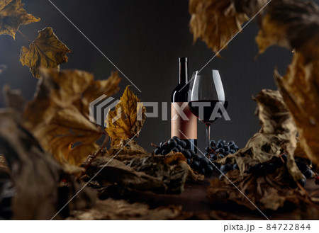 Red wine on a table with dried vine leaves and blue grapes. 84722844