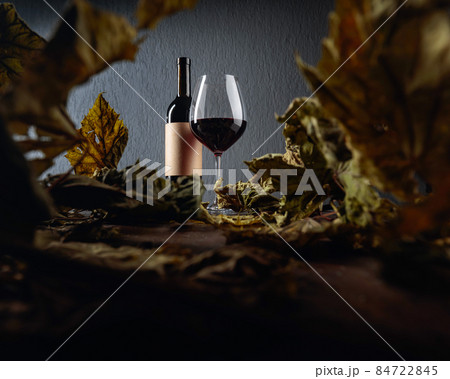 Bottle and glass of red wine on a table with dried vine leaves. Selective focus. 84722845