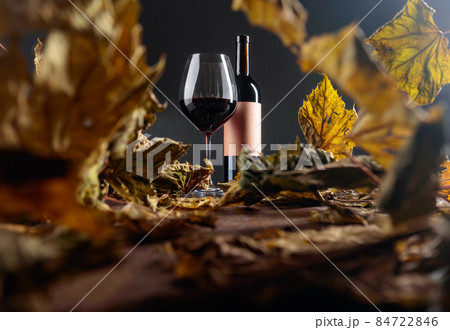 Bottle and glass of red wine on a table with dried vine leaves. Selective focus. 84722846