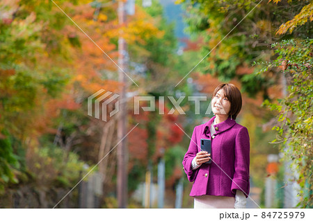 秋の風景の中にいるスマートフォンを持った女性 秋の風景の中にいるスマートフォンを持った女性 84725979