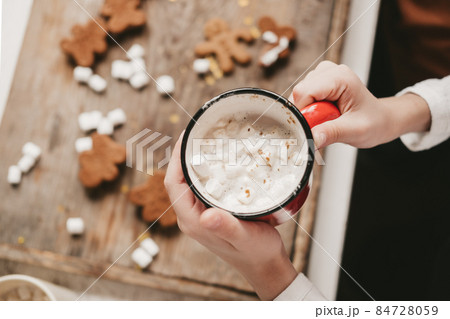a cup of cocoa with marshmallows close-up, against the backdrop of Christmas cookies. Christmas sweets with cocoa and marshmallows for children on a wooden background. Winter vacation at home. 84728059