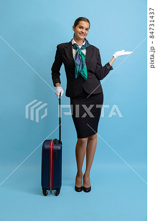 Portrait of beautiful young girl, flight attendant in uniform with suitcase isolated on blue studio background. Portrait of beautiful young girl, flight attendant in uniform with suitcase isolated on blue studio background. 84731437