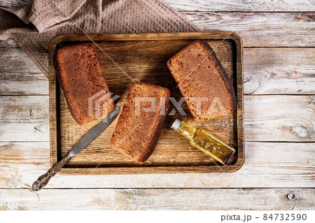 Loafs of rye bread. Fresh homemade bread made from whole grain rye flour. Delicious traditional pastries on a wooden tray on a rustic background. Salt and olive oil. Top view. Copy space Loafs of rye bread. Fresh homemade bread made from whole grain rye flour. Delicious traditional pastries on a wooden tray on a rustic background. Salt and olive oil. Top view. Copy space 84732590