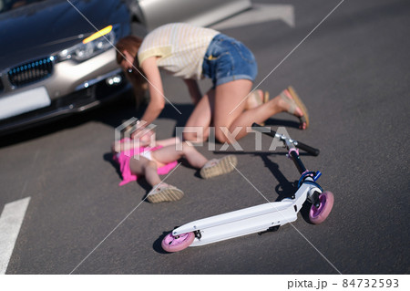 Little girl lying on the asphalt with scooter and her mother after collision with car Little girl lying on the asphalt with scooter and her mother after collision with car 84732593