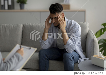 Desperate arab guy suffering from nevrous breakdown, having session at psychologist's office, touching temples 84737844