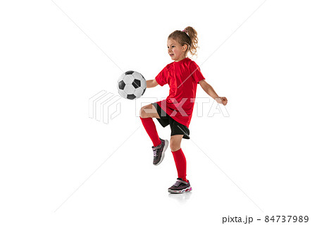 Full-length portrait of girl, child, football player in red uniform training, kicking ball with knee isolated over white background Full-length portrait of girl, child, football player in red uniform training, kicking ball with knee isolated over white background 84737989