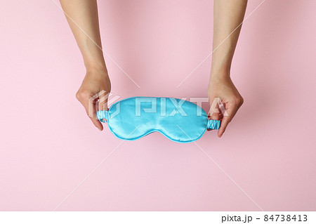 Female hands hold sleep mask on pink background Female hands hold sleep mask on pink background 84738413