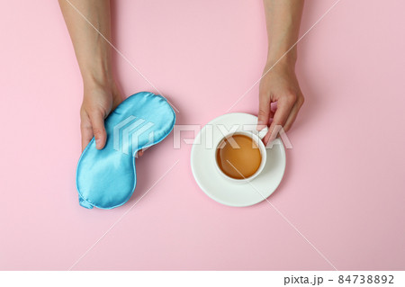 Female hands hold sleep mask and tea on pink background Female hands hold sleep mask and tea on pink background 84738892