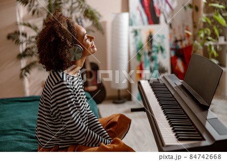 Cheerful young woman sitting near synthesizer at home Cheerful young woman sitting near synthesizer at home 84742668