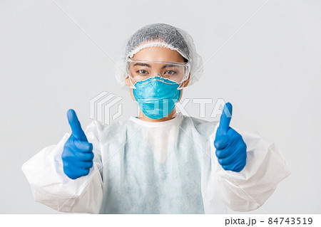 Covid-19, coronavirus disease, healthcare workers concept. Close-up of confident asian female doctor in personal protective equipment showing thumbs-up, recommend or guarantee quality 84743519
