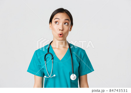 Healthcare workers, preventing virus, quarantine campaign concept. Impressed and amazed asian female doctor, nurse in medical scrubs looking upper left corner pleased, white background 84743531