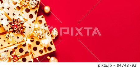 Gift boxes with golden bows, Christmas tree toys and lights on red background. Gift boxes with golden bows, Christmas tree toys and lights on red background. 84743792