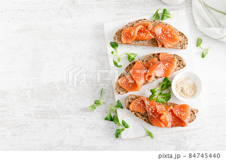 Whole grain rye bread open sandwiches with salted salmon on a white rustic wooden table. Healthy food. Top view Whole grain rye bread open sandwiches with salted salmon on a white rustic wooden table. Healthy food. Top view 84745440