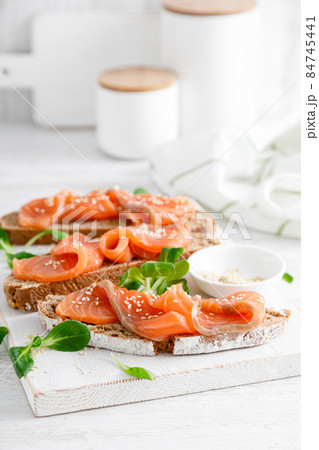 Whole grain rye bread open sandwiches with salted salmon on a white rustic wooden table. Healthy food Whole grain rye bread open sandwiches with salted salmon on a white rustic wooden table. Healthy food 84745441
