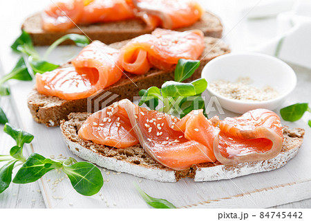 Whole grain rye bread open sandwiches with salted salmon on a white rustic wooden table. Healthy food Whole grain rye bread open sandwiches with salted salmon on a white rustic wooden table. Healthy food 84745442