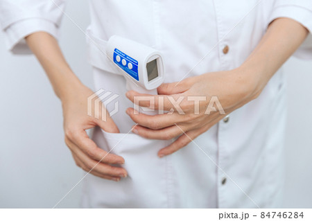 Temperature measurement gun in doctor hands. Close-up shot of doctor wearing protective surgical mask ready to use infrared isometric thermometer gun to check body temperature for virus symptoms. Temperature measurement gun in doctor hands. Close-up shot of doctor wearing protective surgical mask ready to use infrared isometric thermometer gun to check body temperature for virus symptoms. 84746284