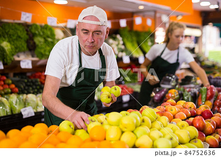 Male seller in uniform holding golden apples 84752636