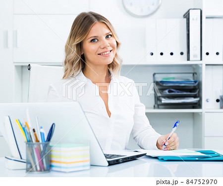 Young woman in clothes is sitting at the table in the office Young woman in clothes is sitting at the table in the office 84752970