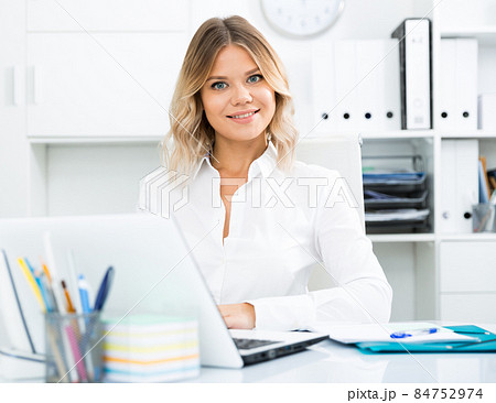 Smiling girl in white shirt sitting at office desk in well-lit office 84752974