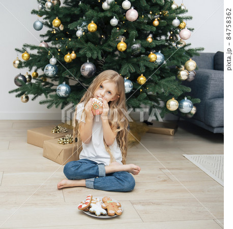 Girl eating Christmas gingerbread near the Christmas tree 84758362