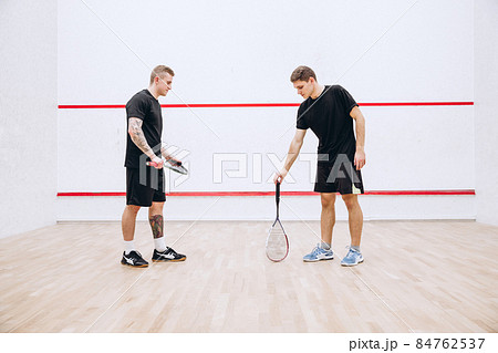 Full-legth portrait of two young sportive men at sport squash studio training, playing team game Full-legth portrait of two young sportive men at sport squash studio training, playing team game 84762537
