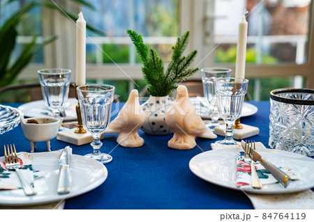 table served with blue tablecloth, pigeons, spruce branches and tableware. 84764119