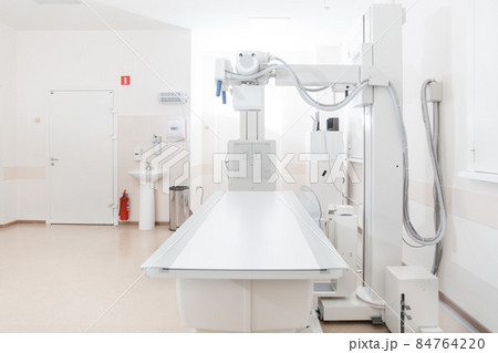 X-ray department in modern hospital. Radiology room with scan machine with empty bed. Technician adjusting an x-ray machine. Scanning chest, heart, lungs in modern clinic office. X-ray department in modern hospital. Radiology room with scan machine with empty bed. Technician adjusting an x-ray machine. Scanning chest, heart, lungs in modern clinic office. 84764220