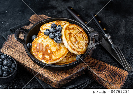 Pancakes with fresh blueberries and maple syrup in a pan. Black background. Top View Pancakes with fresh blueberries and maple syrup in a pan. Black background. Top View 84765254