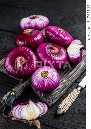 Whole and halfed Flat red sweet onion on a cutting board. Black Wooden background. Top View Whole and halfed Flat red sweet onion on a cutting board. Black Wooden background. Top View 84765315