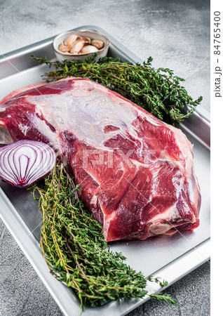 Raw lamb mutton shoulder meat in a baking dish with thyme and garlic. White background. Top view Raw lamb mutton shoulder meat in a baking dish with thyme and garlic. White background. Top view 84765400