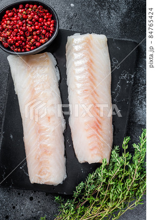 Raw cod loin fillet fish on marble board. Black background. Top view 84765424