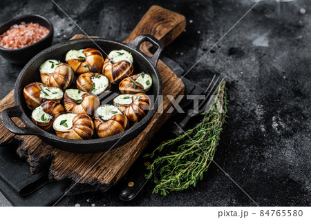 Delicatessen food - Bourgogne Escargot Snails with garlic butter in a pan. Black background. Top view. Copy space 84765580